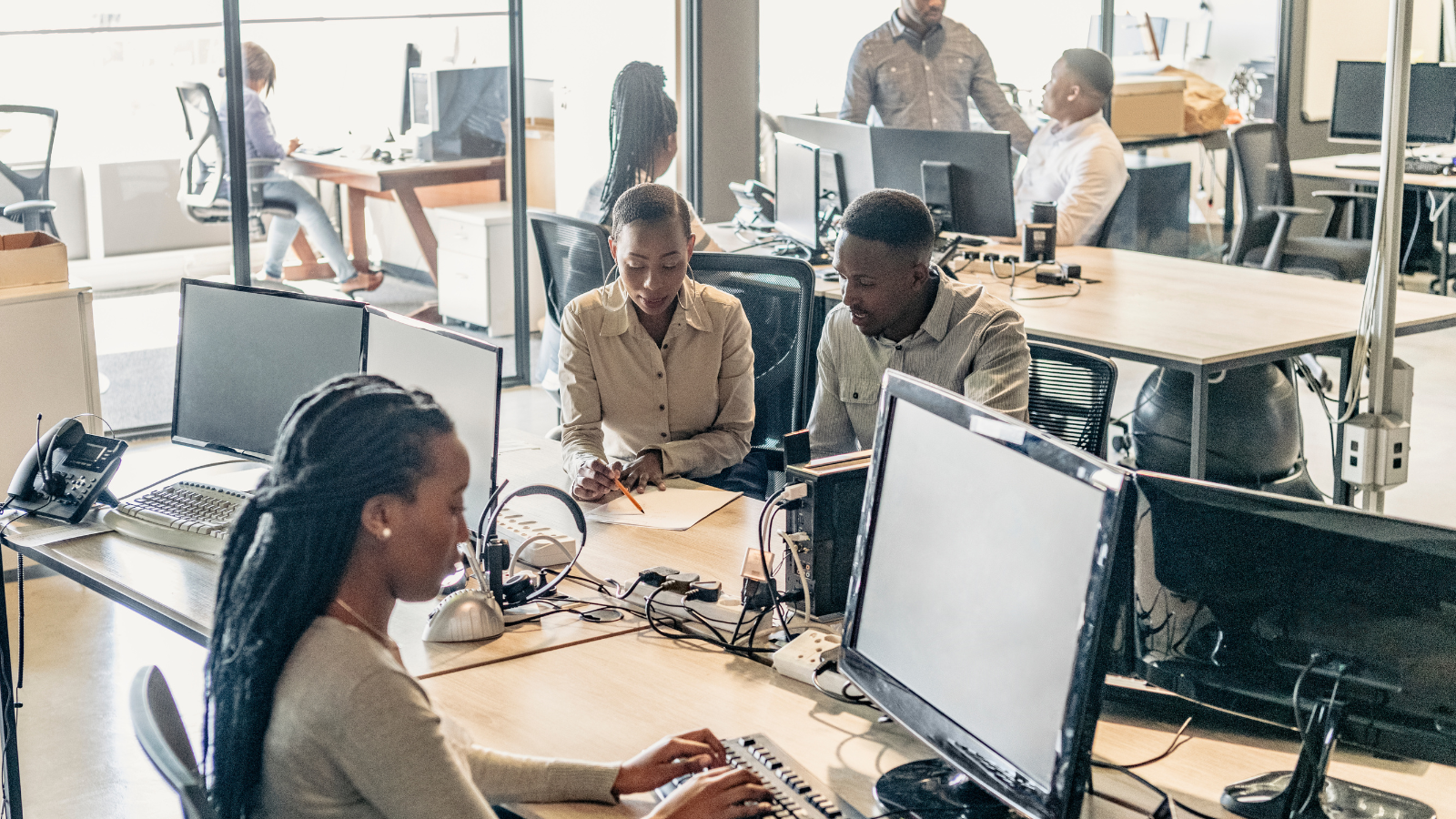 Office setting with various team members working at desks with desktop computers.